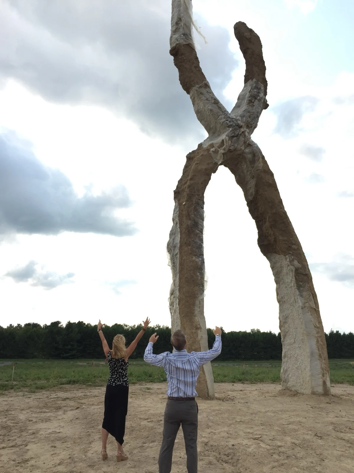 Two figures rising on their own and meeting as one. That is interdependence. | A sculpture of two forms joining into a single arch with Zac Spowart's parents standing beneath, a metaphor for interdependence versus independence in love by Zac Spowart, Love Unlocked.